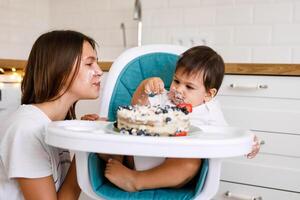 Happy mother with one year old baby celebrating with first birthday with white kitchen on background photo