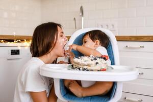 Happy mother with one year old baby celebrating with first birthday with white kitchen on background photo