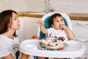 Happy mother with one year old baby celebrating with first birthday with white kitchen on background photo