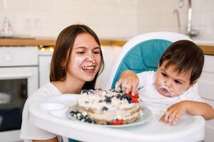 Happy mother with one year old baby celebrating with first birthday with white kitchen on background photo