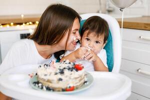 Happy mother with one year old baby celebrating with first birthday with white kitchen on background photo