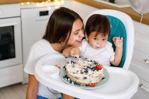 Happy mother with one year old baby celebrating with first birthday with white kitchen on background photo