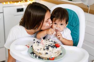 Happy mother with one year old baby celebrating with first birthday with white kitchen on background photo