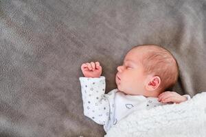 Baby newborn sleeping covered on gray woolen blanket photo