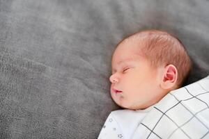 Smiling baby girl lying on a bed sleeping on gray sheets photo