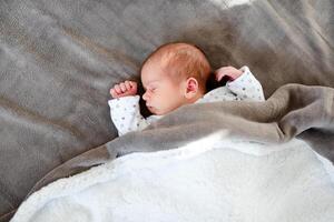 Smiling baby girl lying on a bed sleeping on gray sheets photo