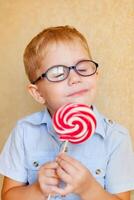 A little boy wearing glasses and having cross-eyes is enjoying a large red candy photo