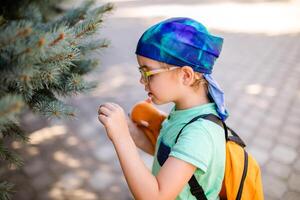 A funny little boy in glasses and a bandana, wearing a green t-shirt and denim shorts, having fun and joking photo
