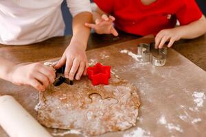 Close-up of children's hands cutting cookies with a cookie cutter on gingerbread dough photo