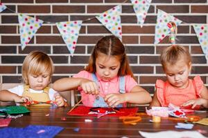 A little toddler boy and two girls cutting something out of beautiful paper at a party photo