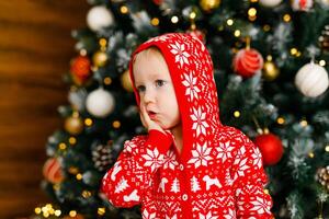 close-up portrait of toddler in red outfit with cute expressions of surprise and joy on background of Christmas tree photo