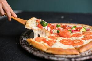 Hot pizza slice with melting cheese on a rustic black table. photo