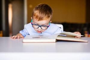 Cute toddler boy with down syndrome with big glasses reading intesting book photo