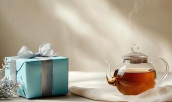 A blue box with a ribbon sits on a table next to a tea pot photo