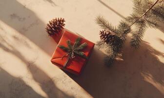 A red box with a green ribbon sits on a table next to pine cones photo
