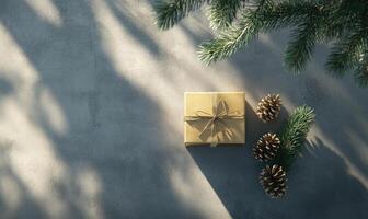 A gold box with a bow on top of a grey surface with pine cones on the right photo
