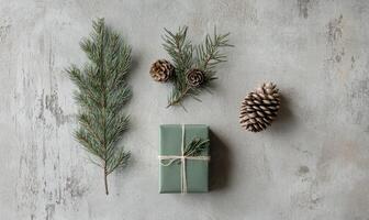 A green box with a ribbon on it is surrounded by pine needles and pine cones photo
