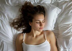 Tranquil young woman lying asleep in bed, top-down view photo