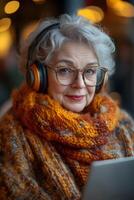 A senior woman enthusiastically attending a virtual class with wireless headphones and a laptop. Her modern, tech-friendly environment adds to the learning vibe. photo