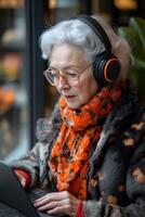 A senior woman enthusiastically attending a virtual class with wireless headphones and a laptop. Her modern, tech-friendly environment adds to the learning vibe. photo