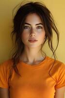 Beautiful young woman in an orange t-shirt, top half body shot, facing the camera against a soft yellow blur background. photo