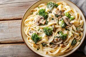 Tagliatelle pasta with creamy sauce, mushrooms, and broccoli served in a bowl photo