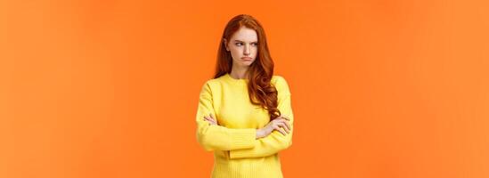 Offended angry and tensed woman with curly red hair, freckles, having bad mood, cross arms chest, thinking troublesome situation, frowning getting mad, standing orange background distressed photo