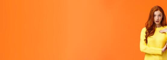 Who me. Frustrated and shocked, confused redhead woman accused, pointing herself and gasping stare astounded, feeling hurt person blame her, receive accusations, orange background photo