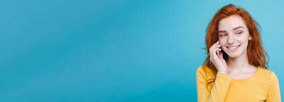 Lifestyle and Technology concept - Portrait of cheerful happy ginger red hair girl with joyful and exciting talking with friend by mobile phone. Isolated on Blue Pastel Background. Copy space photo