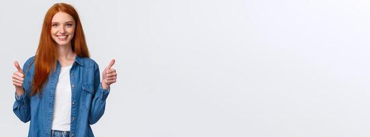 Waist-up portrait alluring confident smiling redhead female blogger review awesome new product, showing thumbs-up in approval, like or agree gesture, standing white background photo