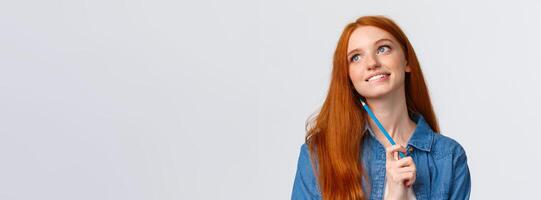 Lovely and creative, thoughtful dreamy smiling redhead woman looking up and thinking, imaging something beautiful, holding colored pencil, drawing, attend art courses, white background photo