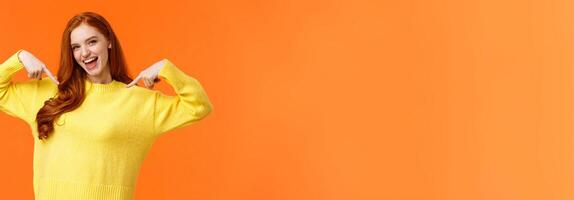 Confident and energized, good-looking redhead woman pointing at herself, introducing personal achievement, bragging or being proud, volunteer, feeling upbeat, smiling, orange background photo