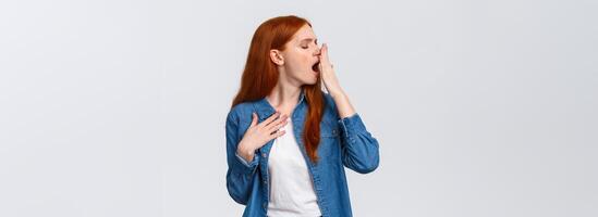 Waist-up portrait lovely redhead girl want sleep, feeling tired or bored, turn head away and yawn, cover opened mouth with palm, yawning over white background after boring class, white background photo