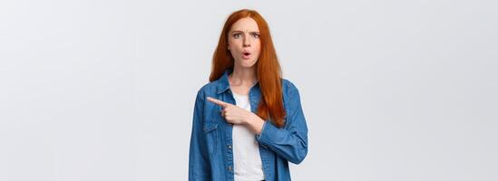 What is that. Displeased, tensed and mad frustrated redhead bossy woman pointing right waiting explanation as staring puzzled and upset, standing white background bothered photo