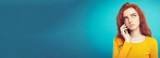 Lifestyle concept - Portrait of ginger red hair girl with shocking and stressful expression while talking with friend by mobile phone. Isolated on Blue Pastel Background. Copy space photo