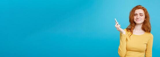 Lifestyle and Technology concept - Portrait of cheerful happy ginger red hair girl with joyful and exciting smiling to camera. Isolated on Blue Pastel Background. Copy space. photo