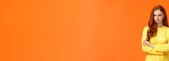 Offended angry and tensed woman with curly red hair, freckles, having bad mood, cross arms chest, thinking troublesome situation, frowning getting mad, standing orange background distressed photo