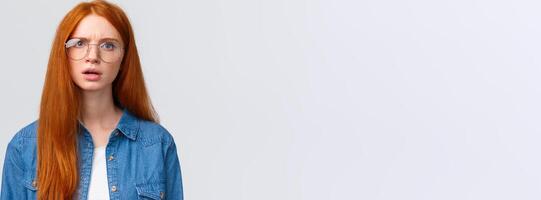Confused and displeased, unsure redhead girl in glasses having conversation, talking look frustrated and slightly unconvinced, have doubts standing white background frowning photo