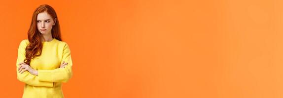 Offended angry and tensed woman with curly red hair, freckles, having bad mood, cross arms chest, thinking troublesome situation, frowning getting mad, standing orange background distressed photo