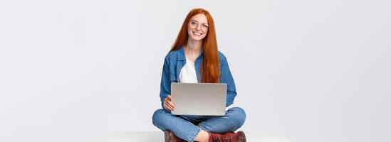 Attractive charismatic redhead caucasian female sit on floor with crossed legs, holding laptop laps, working on fresh air, writing new program, freelancing over white background photo