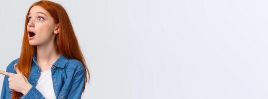 Have you seen it. Close-up astonished and impressed shook redhead girl saw something impressive, open mouth excited, pointing finger left, watching awesome performance, white background photo