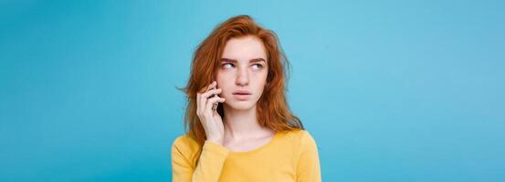 Lifestyle concept - Portrait of ginger red hair girl with shocking and stressful expression while talking with friend by mobile phone. Isolated on Blue Pastel Background. Copy space photo