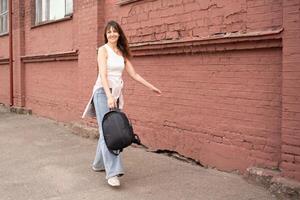 a woman in jeans with a backpack walks cheerfully and quickly down the street. walk in summer, spring in good weather photo