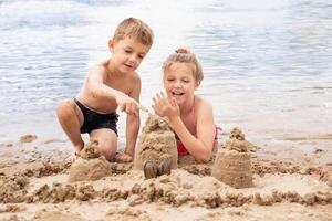 Boy and girl laughing and playing on the nice beach on summer holidays. happy children building a sandcastle at the sea photo