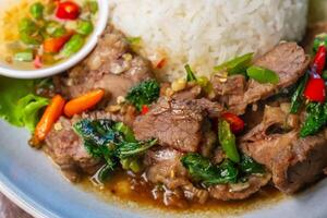 Closeup Stir-fried beef with basil in a blue plate with fish sauce, chili, cucumber and lettuce on a wooden table. photo