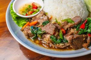 Closeup Stir-fried beef with basil in a blue plate with fish sauce, chili, cucumber and lettuce on a wooden table. photo