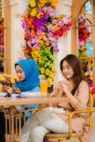 portrait of diversity 2 beautiful young indonesia female smiling praying devoutly before eating sitting on chairs in an indoor restaurant. for the concept of religion, lifestyle, worship, advertising photo