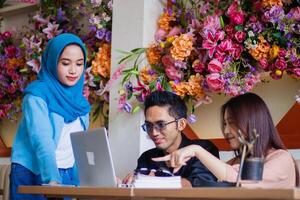 A group of smiling indonesia freelancers are focused on brainstorming and chatting while working on a company assignment in a coffee shop cafe. for group, company, education, business concept photo
