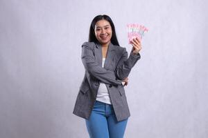 expression of beautiful adult office lady cheerful holding rupiah money wearing gray suit isolated on white background. for giveaway content, lifestyle, prize, event, competition photo