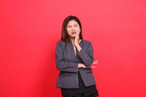 Asian office girl expression in pain, toothache candid, wearing a gray jacket and black mini skirt on a red background. for health, business and advertising concepts photo